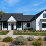 Modern farmhouse custom home in Cache Valley, Utah with white board-and-batten siding, black trim, covered front porch, landscaped yard, native plants, stone accents, and mountain views