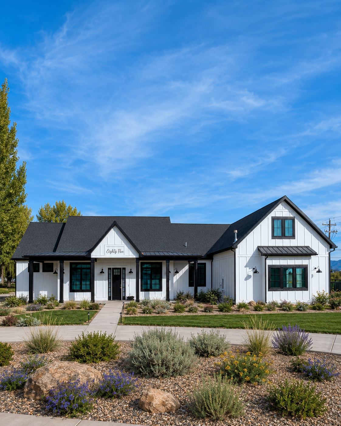 Modern farmhouse custom home in Cache Valley, Utah with white board-and-batten siding, black trim, covered front porch, landscaped yard, native plants, stone accents, and mountain views.