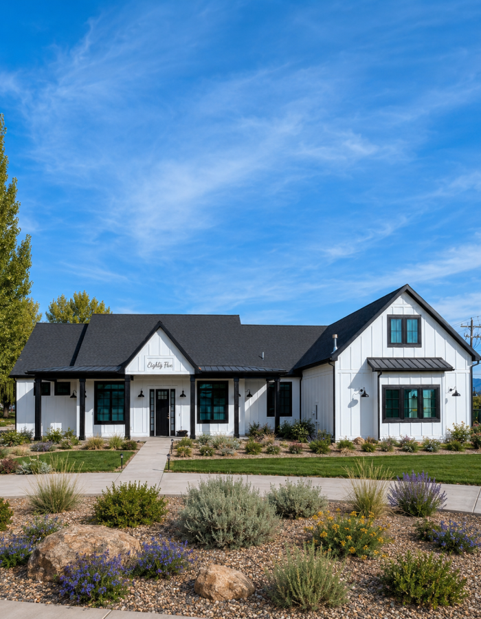 Modern farmhouse custom home in Cache Valley, Utah with white board-and-batten siding, black trim, covered front porch, landscaped yard, native plants, stone accents, and mountain views.